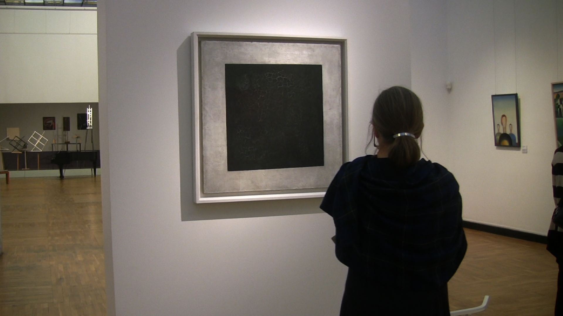 Frau von hinten betrachtet ein schwarzes Quadrat in einem Museumssaal.