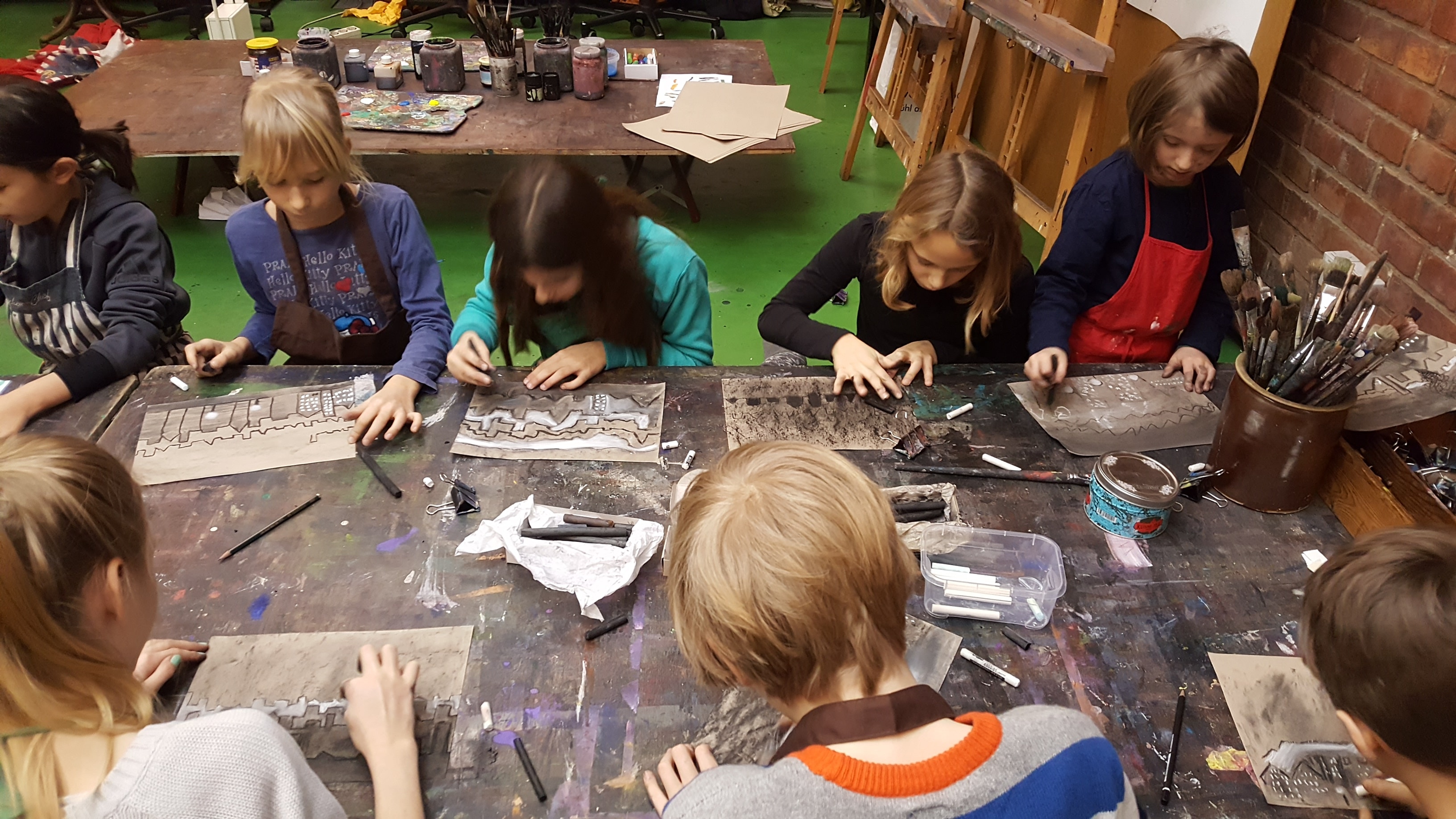 Kinder zeichnen an einem langen Arbeitstisch im Atelier