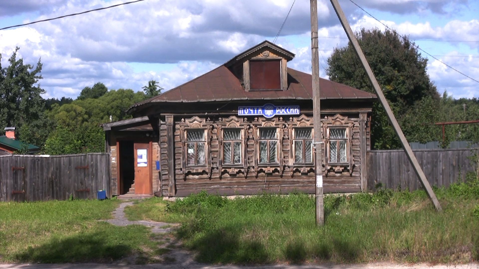 Verziertes Holzhaus mit Schriftzug Post Russlands vor bewölktem Himmel.
