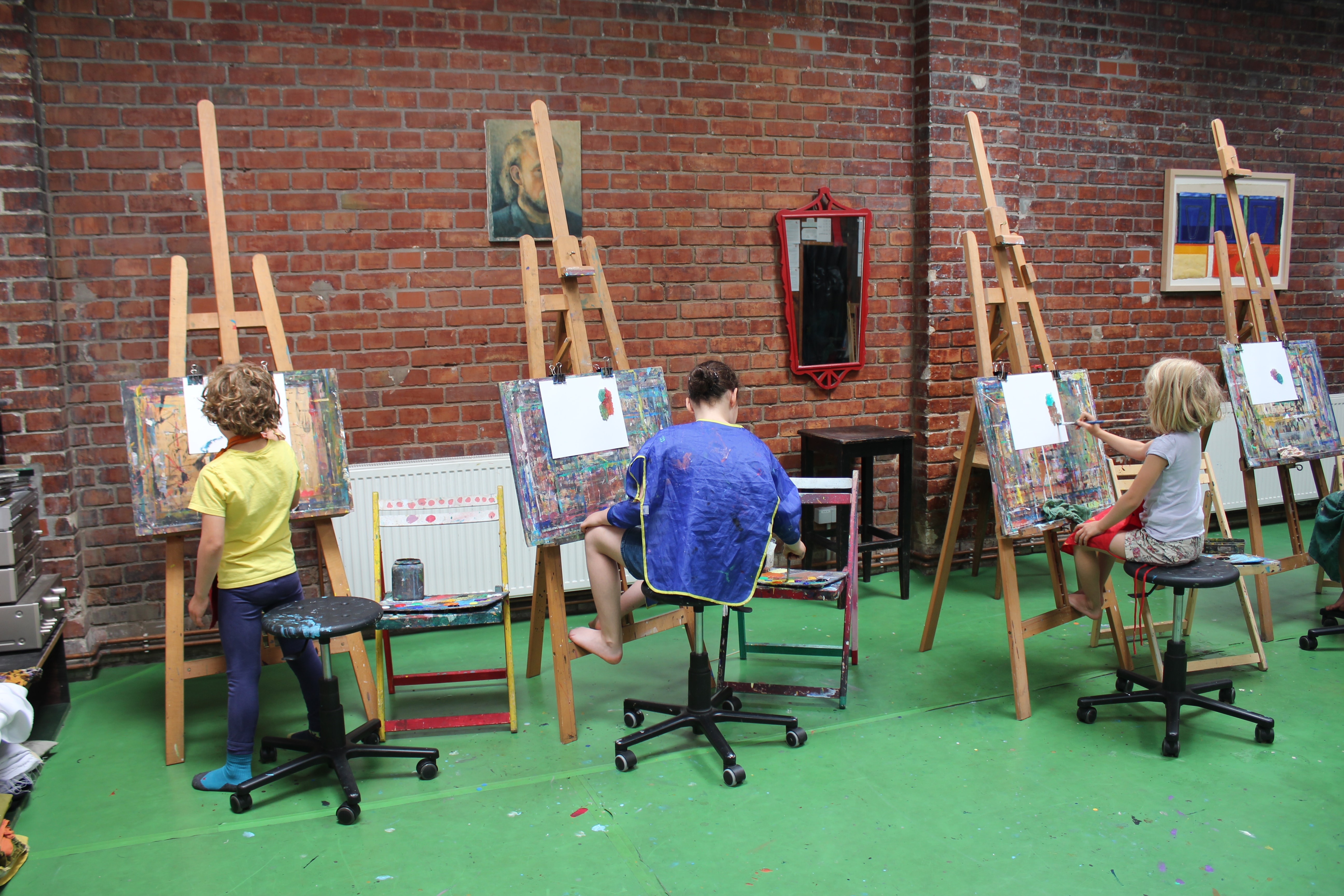 Kinder malen im Atelier an Staffeleien vor einer Backsteinwand