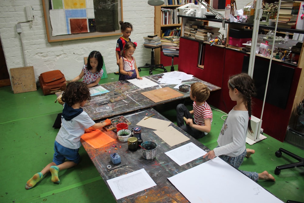 Kinder arbeiten im Atelier am Boden und an niedrigen Tischen